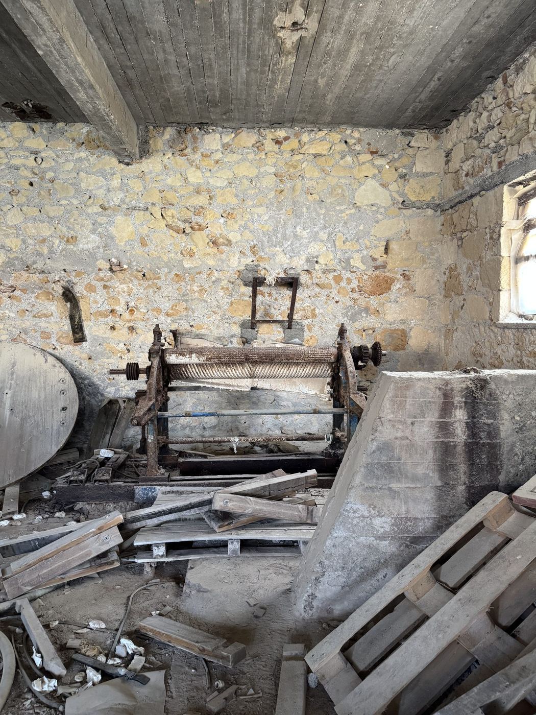 Inside an abandoned tannery: a rusted fleshing machine against a rubble stone wall, timber and debris across the floor