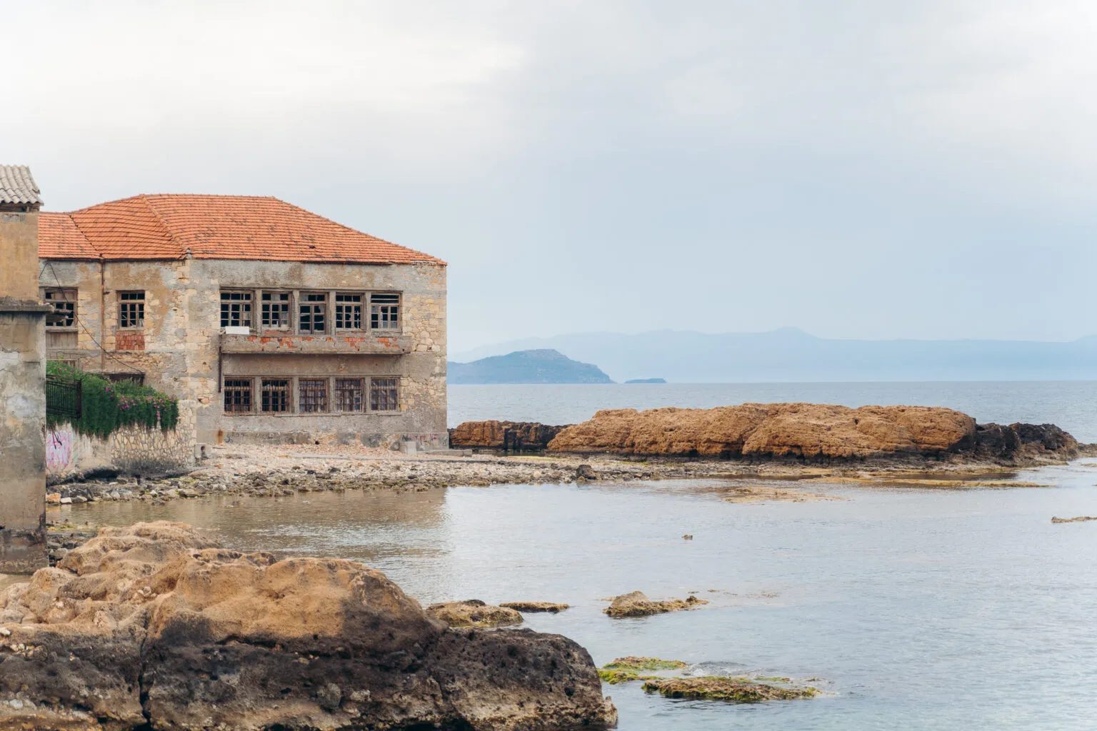 A tannery on the rocks at Tabakaria, its long seaward elevation with two ranks of broken windows under a tiled roof, the Cretan sea beyond