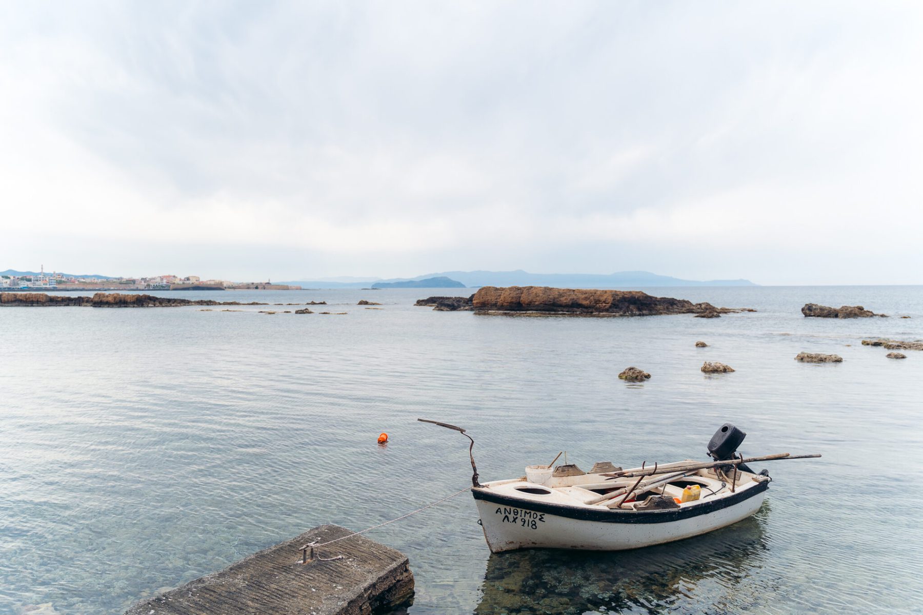 A small wooden fishing boat moored in shallow water off flat rocks, the town on the horizon